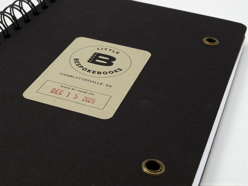 Inside back cover of the Little Bespokebooks Reading Journal showing signature “Made by hand on” label stamped in red ink with date December 15, 2025. Black cover with antique brass grommets and rounded corners. Label includes Little Bespokebooks logo and Charlottesville, Virginia mark.