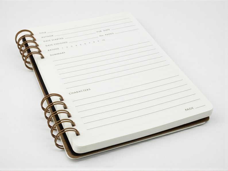 Reading journal open to a single review page with spaces for title, author, dates, rating, summary, and characters, shown at an angle against a white background.