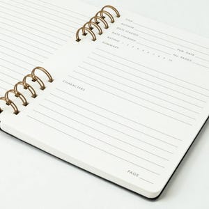 Close angled view of reading journal open to a full spread, showing the book details page in the foreground and the notes and reflections page in the background. Dual antique brass wire binding is visible.