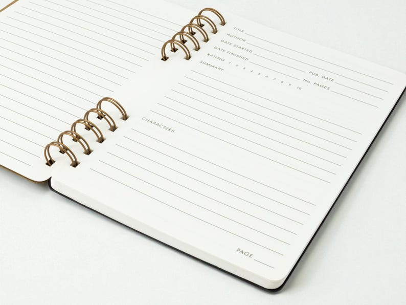 Close angled view of reading journal open to a full spread, showing the book details page in the foreground and the notes and reflections page in the background. Dual antique brass wire binding is visible.
