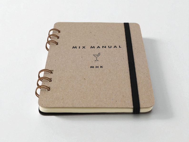 Mix Manual cocktail recipe journal with kraft chipboard cover, bronze wire binding, and black elastic band, shown closed on white background — handmade cocktail recipe notebook