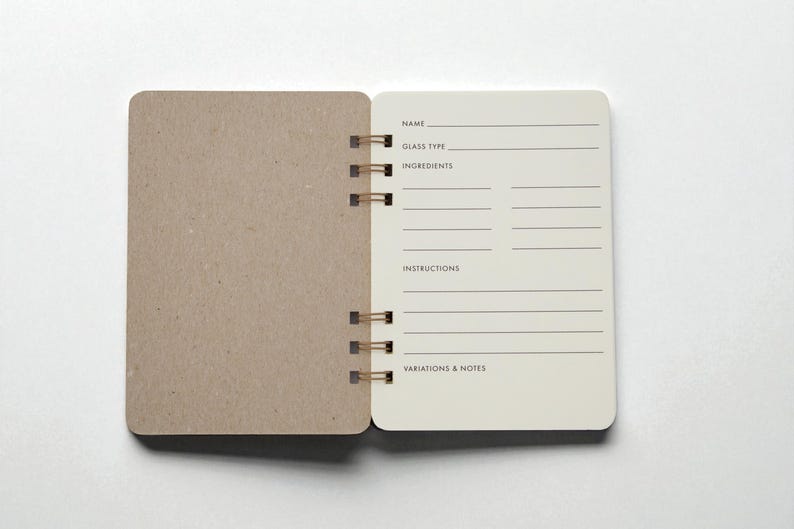 Open Mix Manual cocktail recipe journal with structured ivory colored drink recipe pages for name, glass type, ingredients, instructions, and notes — handmade bar notebook