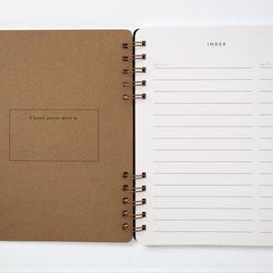 Inside pages of handmade book journal open to the index spread. Left interior cover of journal includes an “If found, please return to” box. Right-hand page has lined index to record book titles and page numbers. Bound with antique brass wire, archival-quality ultrawhite paper.