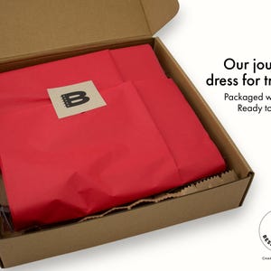 Open shipping box with Little Bespokebooks journal wrapped in red tissue paper and sealed with branded sticker, showing premium packaging presentation for handmade personalized journals from Charlottesville, Virginia.