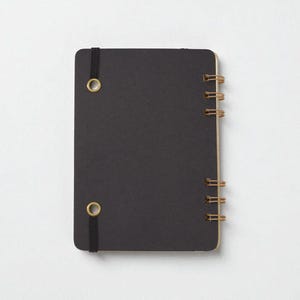 Back cover of Mix Manual cocktail recipe journal in black chipboard with bronze wire binding and black elastic band — handmade bartender notebook
