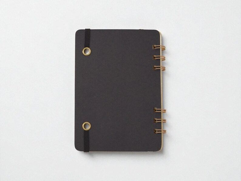 Back cover of Mix Manual cocktail recipe journal in black chipboard with bronze wire binding and black elastic band — handmade bartender notebook