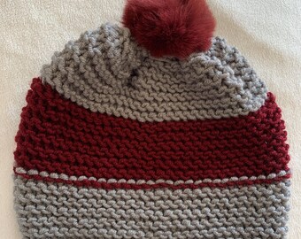 Peut inclure: Bonnet en tricot gris et bordeaux avec un pompon en fausse fourrure bordeaux sur le dessus.