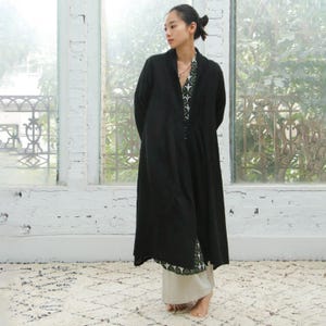 May include: A black long-sleeved shirt with a button-up front and a collar. The shirt is worn over a patterned shirt with a black and white design.