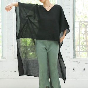 May include: A black, long, sheer top with a V-neckline and wide sleeves. The top is paired with green, wide-leg pants.