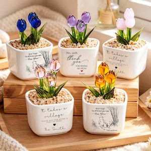 May include: Five small, white square ceramic pots with colourful glass tulip flowers. Each pot has a different message and illustration. The tulips are blue, purple, pink, and yellow. The pots sit on a wooden tray.