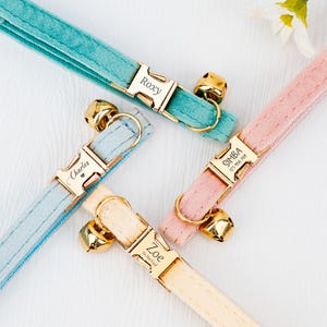 May include: Four personalized cat collars with gold buckles and bells. The collars are in turquoise, light blue, pink, and beige.