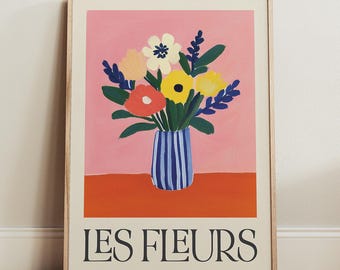 May include: A framed print with a pink background featuring a bouquet of colorful flowers in a blue and white striped vase. The text "LES FLEURS" is printed in black at the bottom of the print.