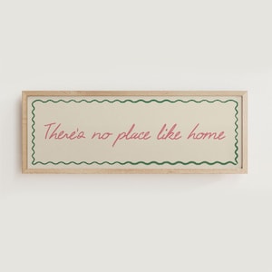 May include: A rectangular wooden framed sign with the text "There's no place like home" in pink script. The text is inside a cream-colored rectangle with a green wavy border.