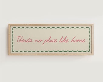 Puede incluir: Un letrero rectangular con marco de madera con el texto "There's no place like home" en escritura rosa. El texto está dentro de un rectángulo color crema con un borde verde ondulado.