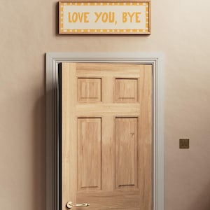 May include: A wooden door with a brass door handle and a framed sign above it that reads "LOVE YOU, BYE" in yellow letters on a white background.