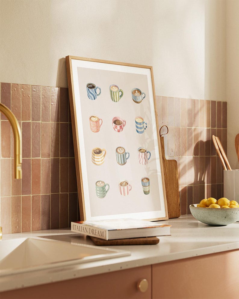 May include: A framed print featuring watercolor illustrations of various coffee mugs. The mugs are in different colors and patterns, including stripes and floral designs. The print is leaning against a wall in a kitchen setting.