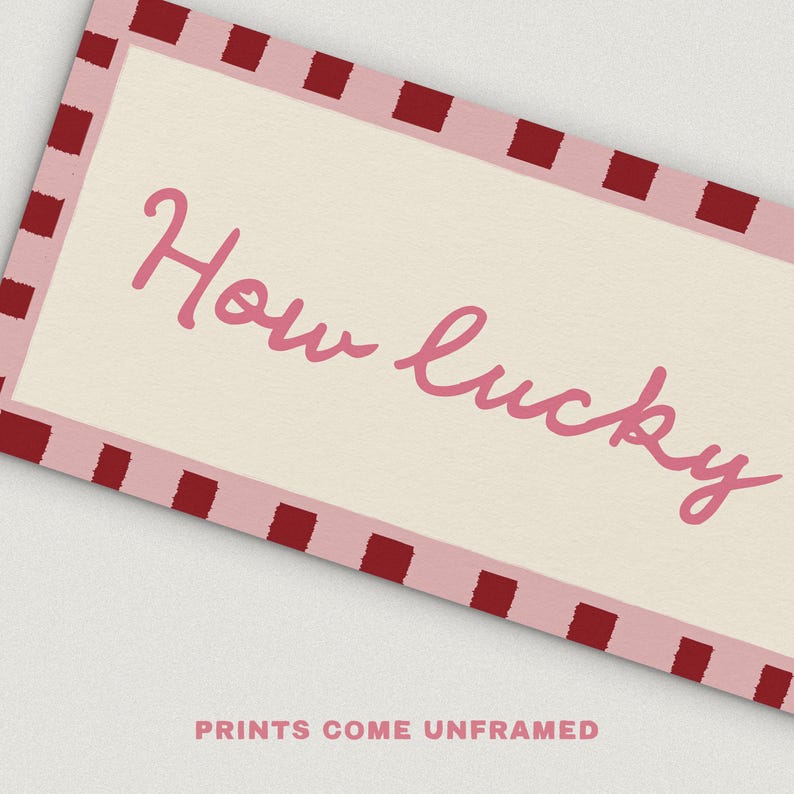 Pu&ograve; includere: Stampa rettangolare con sfondo color crema e bordo rosa con quadrati rosso scuro. Le parole "How lucky" sono scritte in rosa in corsivo. Il testo "PRINTS COME UNFRAMED" &egrave; in basso.