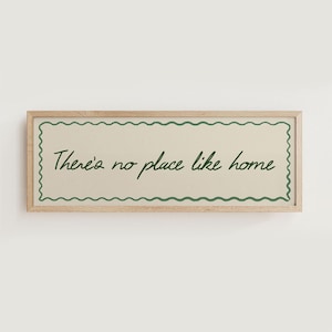 May include: A rectangular wooden framed sign with the phrase "There's no place like home" in green script. The sign has a cream-colored background with a green wavy border.