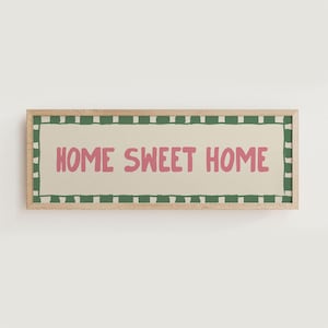 May include: A framed wall art print with a green and white striped border. The print features the text "Home Sweet Home" in pink lettering on a beige background.