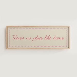 May include: A rectangular wooden framed sign with the text "There's no place like home" in pink script. The text is centered on a cream-colored background with a pink wavy border.