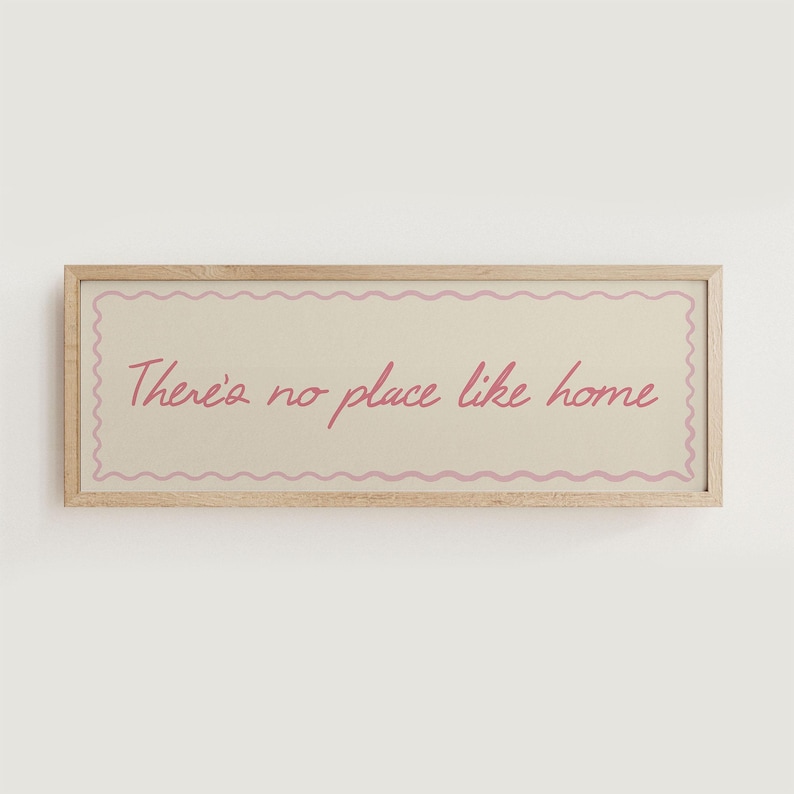 May include: A rectangular wooden framed sign with the text "There's no place like home" in pink script. The text is centered on a cream-colored background with a pink wavy border.