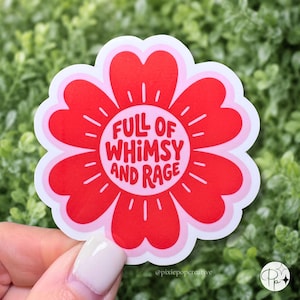 May include: A flower-shaped sticker with a white border, featuring a bright red petal design and a light pink center. The text 'FULL OF WHIMSY AND RAGE' is printed in bold red letters in the middle, surrounded by small white line accents.