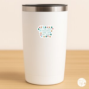 May include: A white insulated tumbler with a silver rim. The tumbler has a sticker with the text "It's the most stressful time of the year" in teal and red, surrounded by snowflakes, hearts, and Christmas trees.