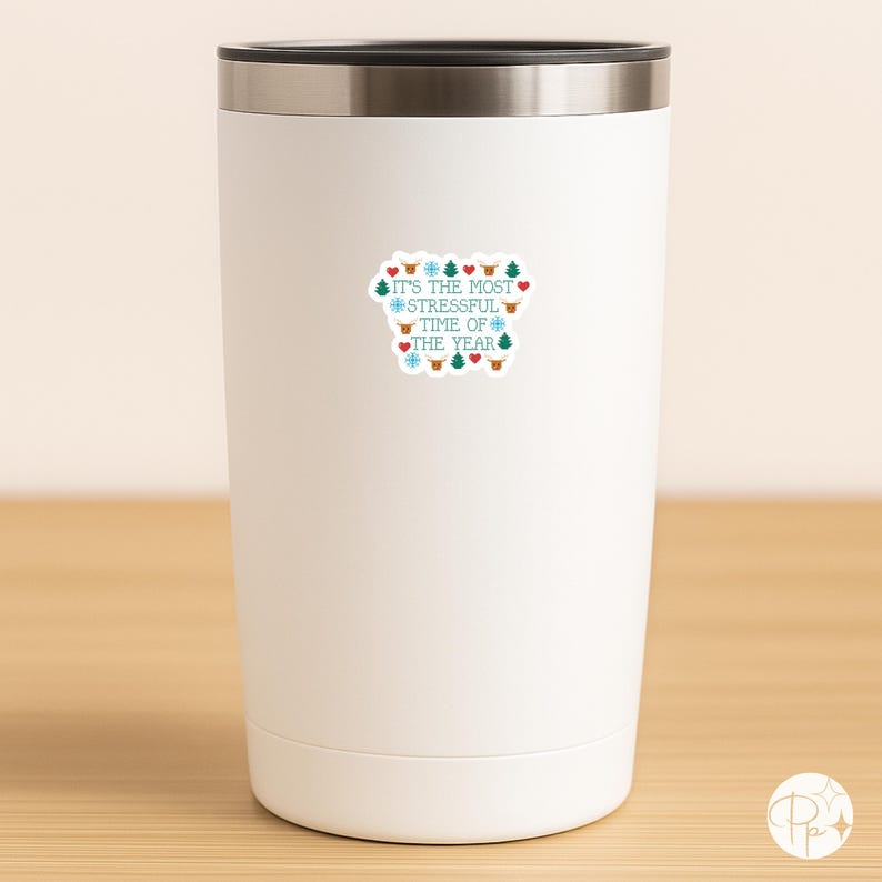 May include: A white insulated tumbler with a silver rim. The tumbler has a sticker with the text "It's the most stressful time of the year" in teal and red, surrounded by snowflakes, hearts, and Christmas trees.