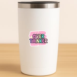 May include: A white stainless steel tumbler with a metallic rim featuring a central sticker. The sticker has a pink background with small stars and the text OVER THINKER in multi-colored, bold, outlined letters with a black border.