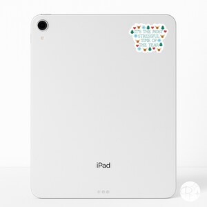 May include: A white iPad with a sticker that reads "IT'S THE MOST STRESSFUL TIME OF THE YEAR" in teal and red. The sticker features Christmas-themed icons like snowflakes, hearts, and reindeer.