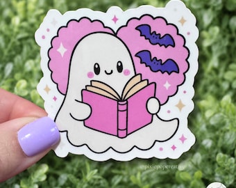 Autocollant d'Halloween pour les amoureux des livres : Fantôme rose en train de lire avec des chauves-souris violettes