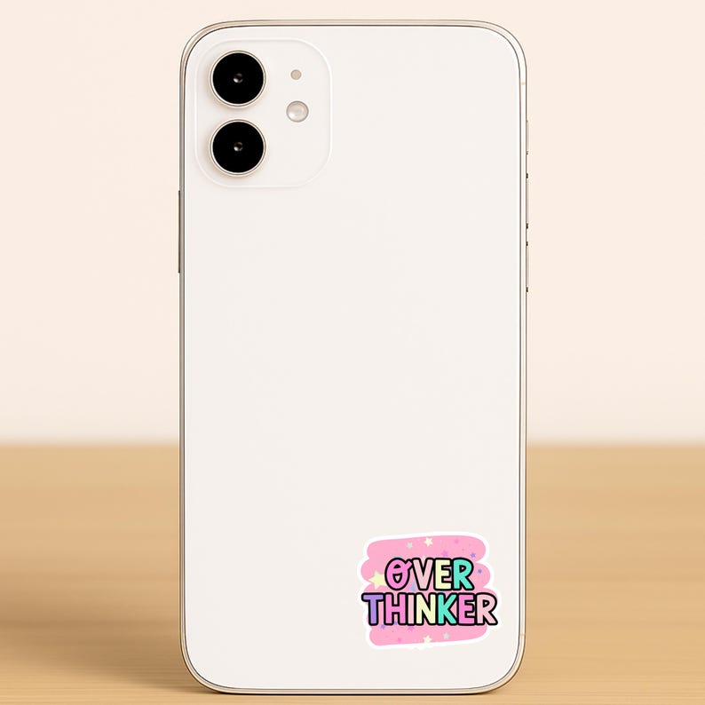 May include: A white smartphone with a rectangular sticker on the back. The sticker features a pink background with small white stars and the text "OVER THINKER" in bold, multi-colored letters with a thick white outline and a dark blue border.