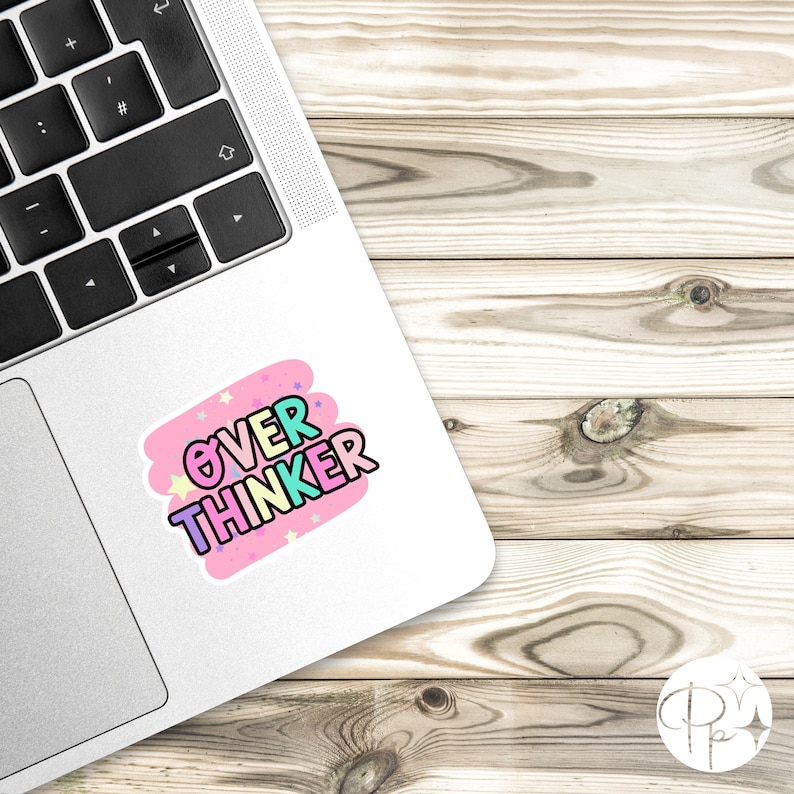 May include: A rectangular sticker applied to the silver surface of a laptop. The sticker features a pink background with small stars and the text OVER THINKER in bold, colorful, bubble-style letters with a black outline and a light blue fill.