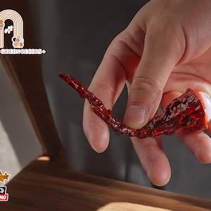 Könnte beinhalten: Eine rote, getrocknete Chilischote mit einem weißen, runden Objekt im Inneren. Die Chilischote wird in einer Hand gehalten.