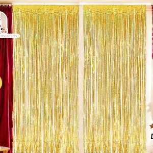 May include: Two gold metallic tinsel curtains hanging in a doorway. The curtains are made of thin strips of shiny gold foil. The text "FESTIVE GILDON DECORS" is visible in the top left corner of the image.