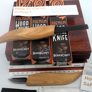 May include: A wood carving kit with a wooden-handled carving knife, a ruler, and several boxes labeled "Premium Wood Carving" and "BeaverCraft." The kit includes a black blade protector and a bandage. The text "How to Carve Safely?" is also visible.