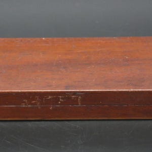 May include: A rectangular wooden storage box with a smooth, reddish-brown finish. The box features a hinged lid and two small, metallic, silver-toned latches on the front edge for securing the closure. The surface shows minor signs of wear.