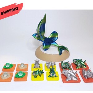 Könnte beinhalten: Ein Set mit 10 bunten Plastikfiguren von Meeresbewohnern, darunter ein fliegender Fisch, ein Fisch mit grün-blauem, schimmerndem Finish und ein silberner Fisch. Die Figuren stehen auf kleinen quadratischen Sockeln mit grünen und orangen Akzenten. KOSTENLOSER VERSAND IN DER EU.