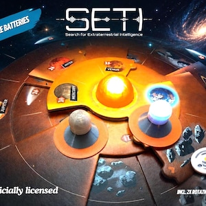 Könnte beinhalten: Ein Brettspiel mit dem Titel SETI: Search for Extraterrestrial Intelligence, bestehend aus einem kreisförmigen orangefarbenen Spielbrett mit Planetenmarkierungen wie Merkur, Venus, Jupiter und Saturn. Das Spiel enthält ein zentrales Licht und zwei Spielsteine.