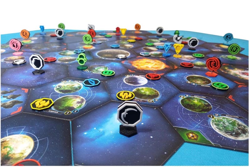 May include: A board game featuring a hexagonal space map with printed planet illustrations and various colored plastic tokens. The game board consists of dark blue space tiles with grid lines, while upright markers in red, yellow, green, and black stand on top.