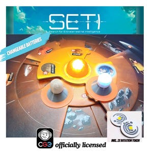 Op de afbeelding: Een close-up van een bordspel genaamd SETI: Search for Extraterrestrial Intelligence. Het bord heeft een cirkelvormig ontwerp met planeten en een centrale zon. Het spel bevat twee witte en grijze rotatietokens.