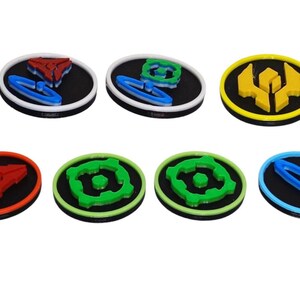 May include: A collection of ten circular tokens featuring raised geometric designs in various colors including red, blue, green, and yellow. Each token has a black base with a colored rim and a central three-dimensional shape on the surface.