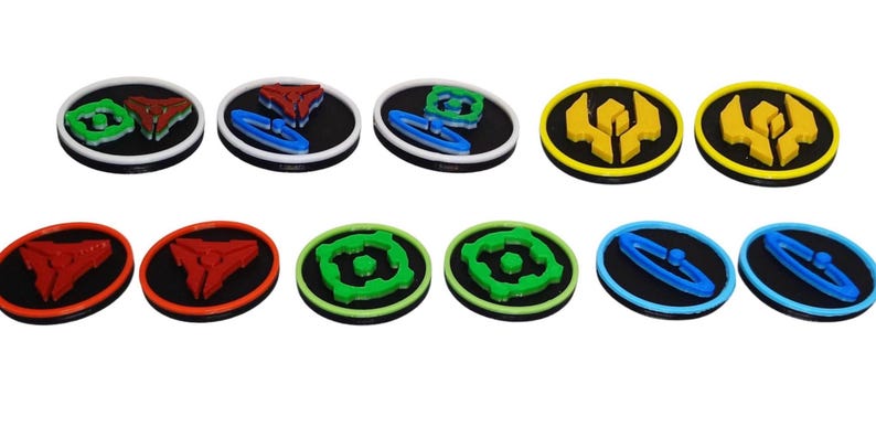 May include: A collection of ten circular tokens featuring raised geometric designs in various colors including red, blue, green, and yellow. Each token has a black base with a colored rim and a central three-dimensional shape on the surface.