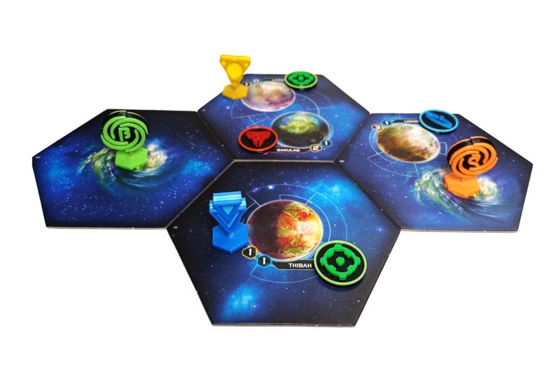 May include: A board game setup featuring three hexagonal space-themed tiles with dark blue galaxy backgrounds. The tiles display planetary illustrations, including one labeled Thibah. Various colored plastic game pieces and tokens are placed on top.