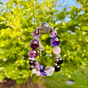 May include: A multi-colored beaded bracelet with a silver charm. The bracelet features amethyst, clear quartz, black obsidian, and labradorite beads.
