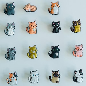 May include: A collection of cat-shaped charms in various colors and patterns. The charms include black, gray, orange, and calico cats, each with unique facial features and poses. These decorative charms are suitable for shoes or other accessories.