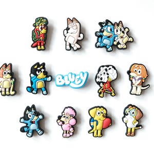 May include: A selection of colourful Bluey character charms. The charms depict various characters in different poses and outfits. The word "Bluey" is written in blue and white. These charms are likely for shoes or accessories.