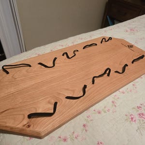 May include: A wooden serving tray with a natural finish and black elastic bands attached to the surface. The tray has an octagonal shape and is made of wood.