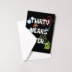 K&ouml;nnte beinhalten: Eine schwarze Gru&szlig;karte mit dem Text "THIRTY YEARS LATER..." in farbenfrohen, verspielten Buchstaben, mit cartoonartigen Blasen und Meeresmotiven. Die Karte steckt teilweise in einem wei&szlig;en Umschlag.