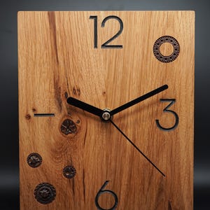 May include: A wooden clock with black Roman numeral hour markers and black hands. The clock face is surrounded by small metal gears.